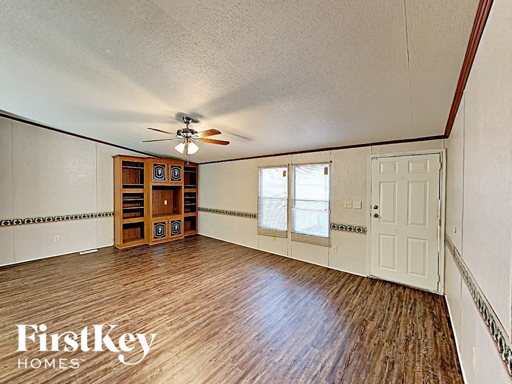 an empty living room with wood floors and a ceiling fan