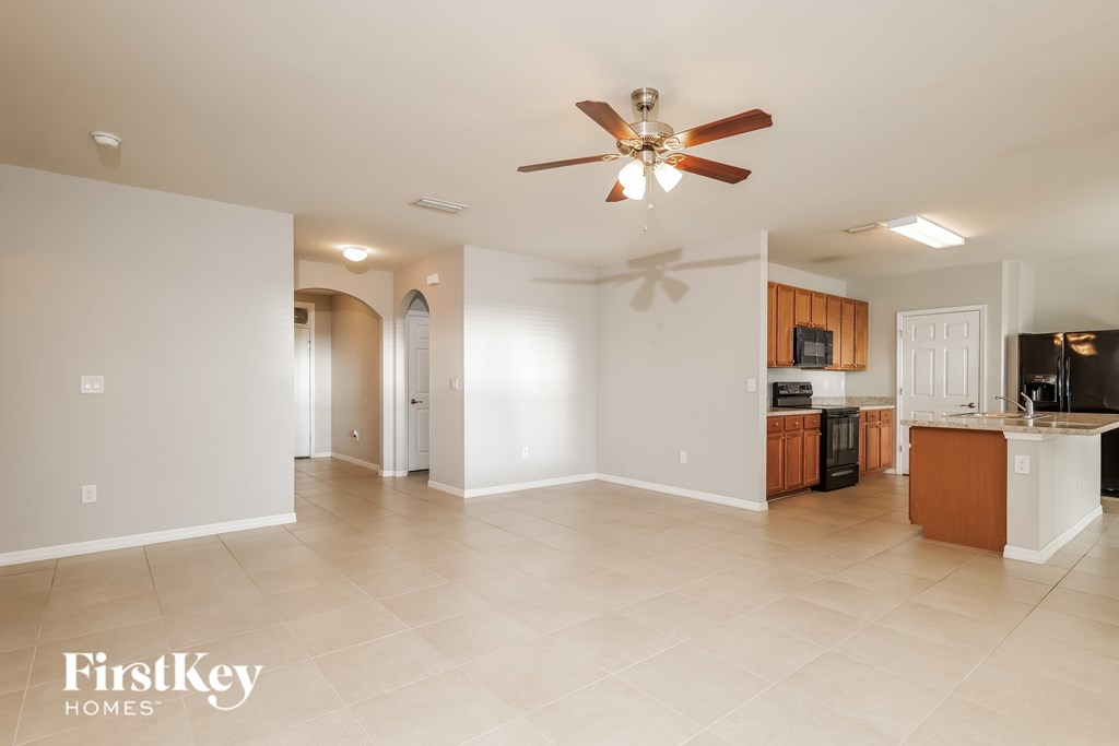 A spacious living room with a ceiling fan and a kitchen area in the background.