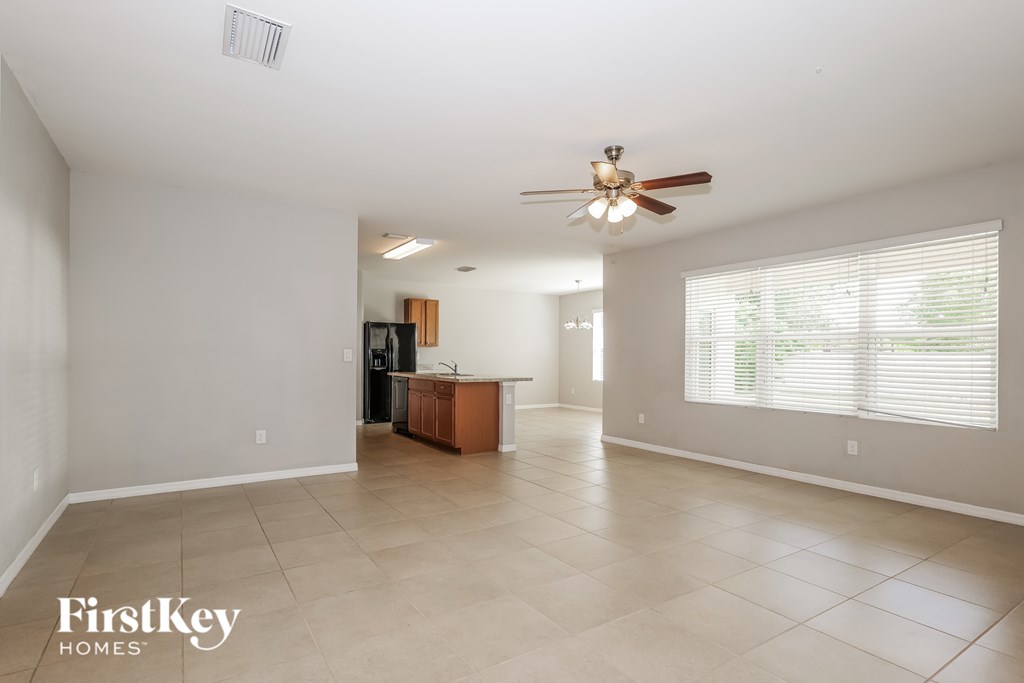 A spacious living room with a ceiling fan and a kitchen area in the background.