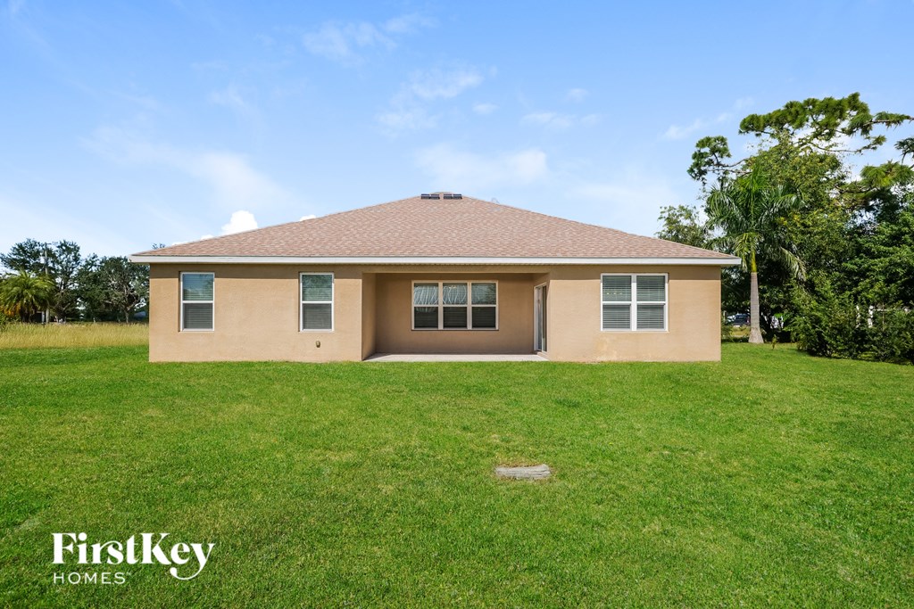 A house with a brown roof and beige walls is surrounded by a grassy lawn.