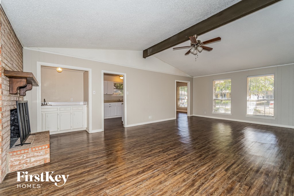 A spacious room with wooden floors and a brick fireplace.