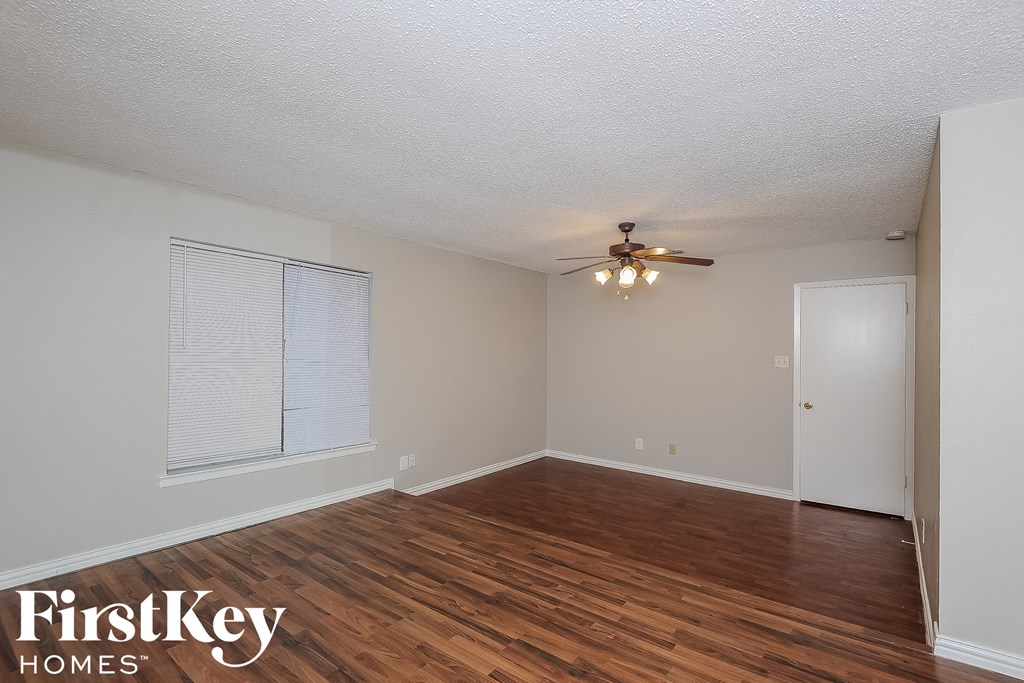 the spacious living room with hardwood flooring and a ceiling fan