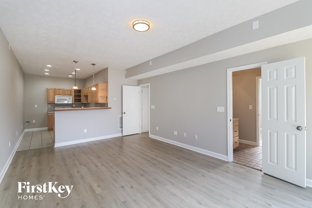 A spacious room with a kitchen area in the background and a doorway leading to another room.