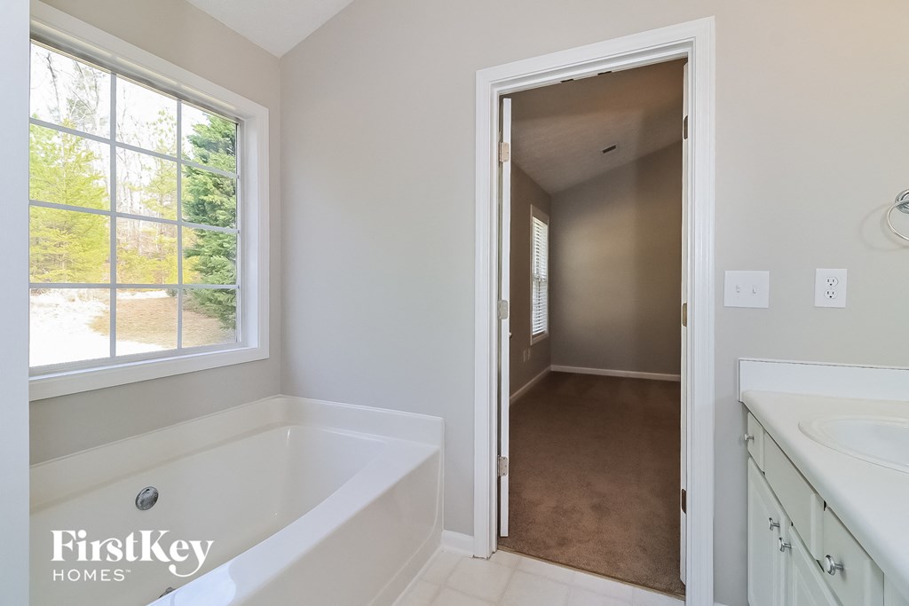 A white bathroom with a tub and a doorway leading to another room.