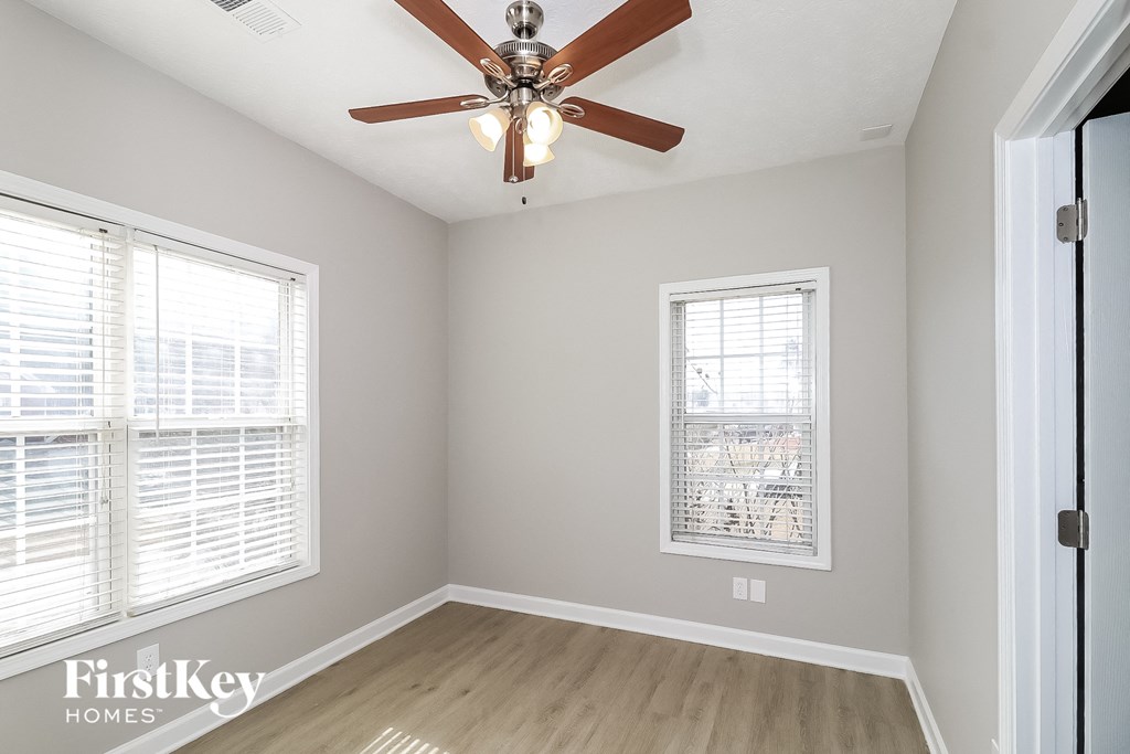 A room with a ceiling fan and two windows.