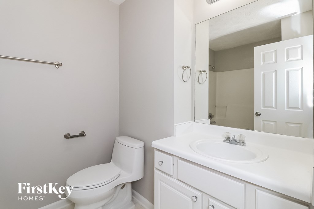 A white bathroom with a toilet, sink and mirror.