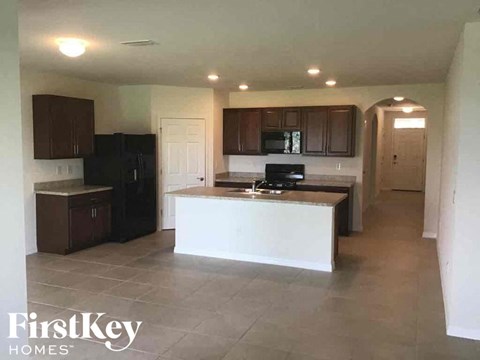 A kitchen with a black fridge and microwave, brown cabinets, and a white island.