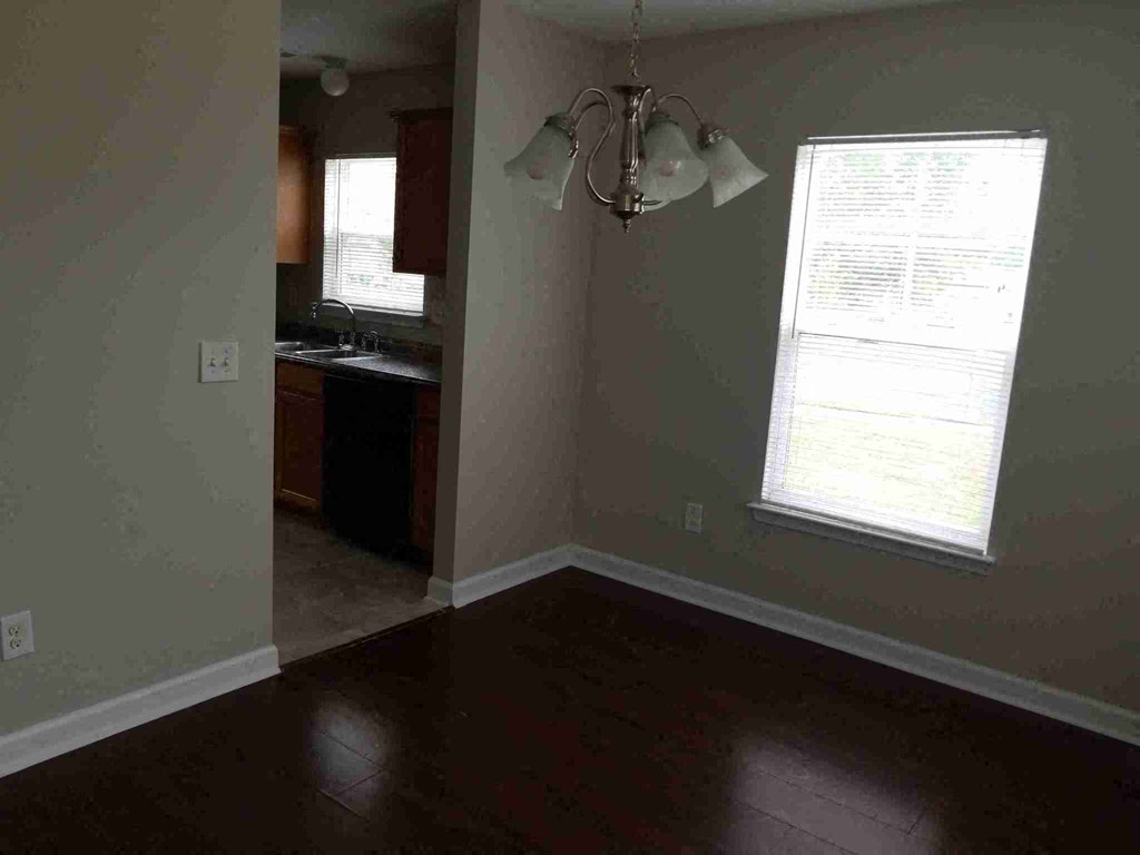 an empty living room with a chandelier and a kitchen