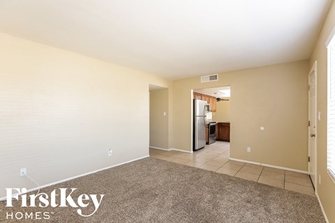 A spacious room with a carpeted floor and a refrigerator in the corner.