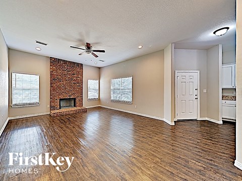 A spacious room with a brick fireplace and wooden floors.