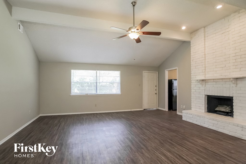 an empty living room with a brick fireplace and a ceiling fan