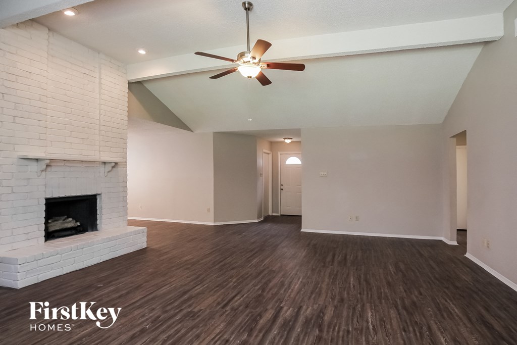 an empty living room with a brick fireplace and a ceiling fan