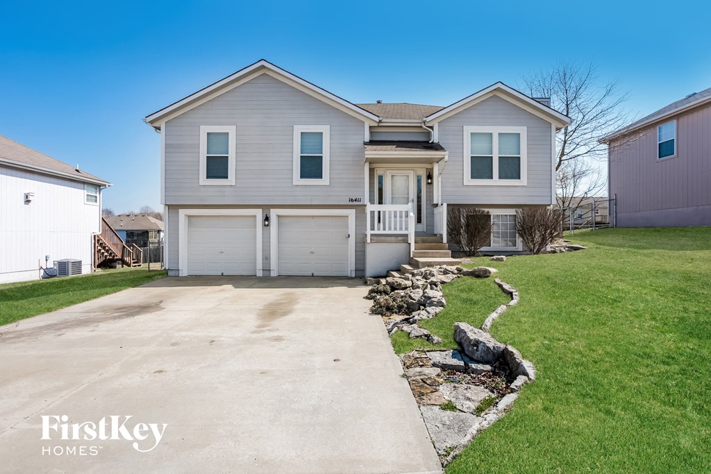 a white house with a driveway and a rock wall in front of it