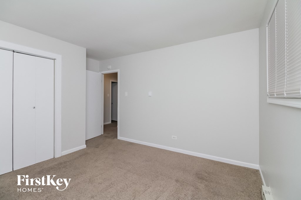 a bedroom with white walls and carpet and a door to a closet