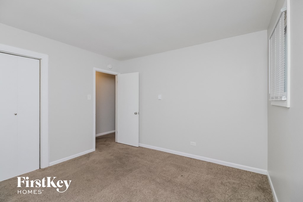 a bedroom with white walls and carpet and a door to a closet