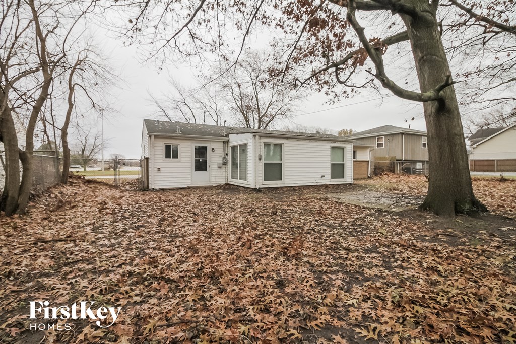 a small white house in a yard with leaves on the ground