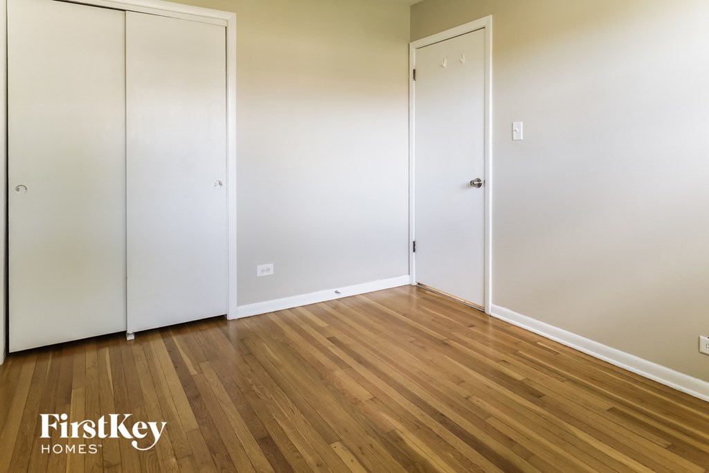 a bedroom with white walls and wood floors and a closet