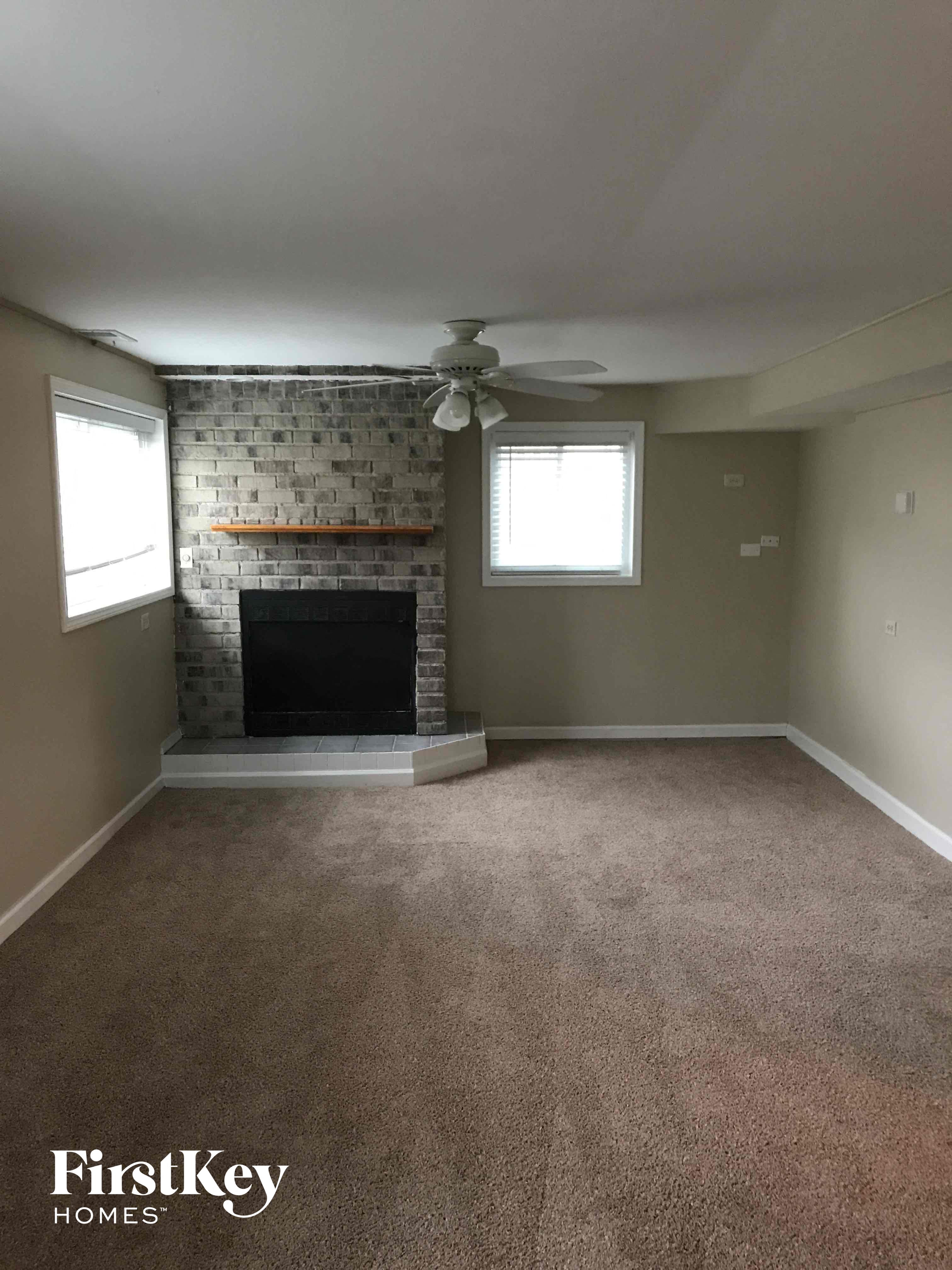 an empty living room with a brick fireplace and a ceiling fan