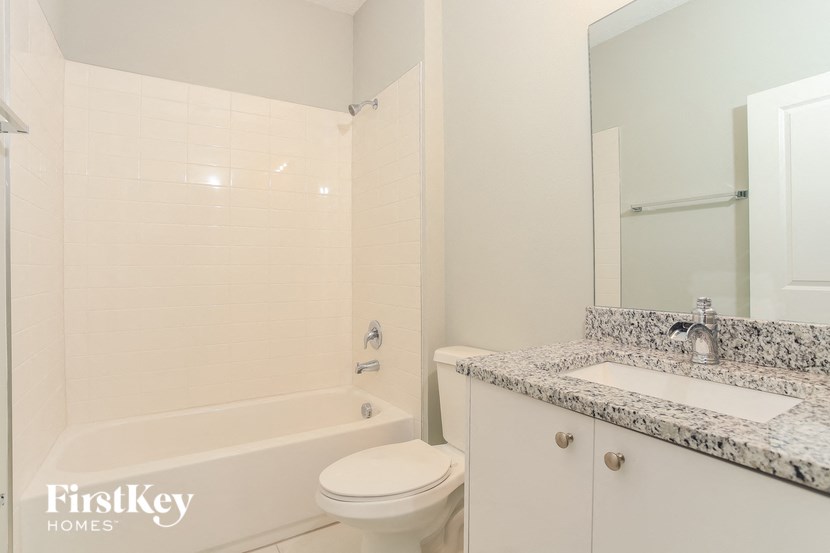 A white bathroom with a marble counter top and a white tub.