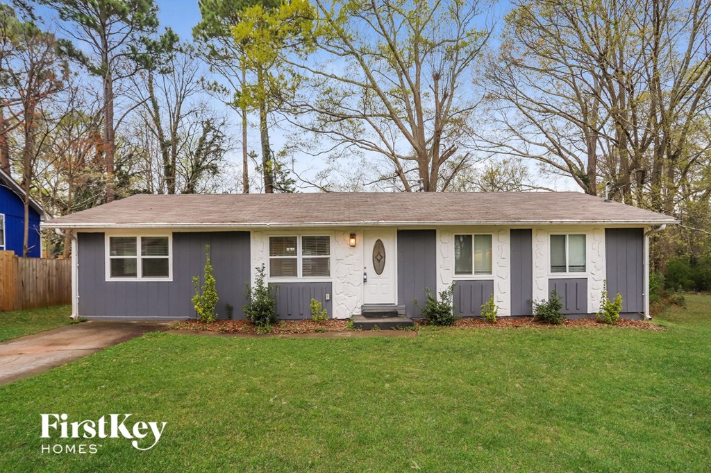 A house with a grey roof and a white door is surrounded by a grassy area.