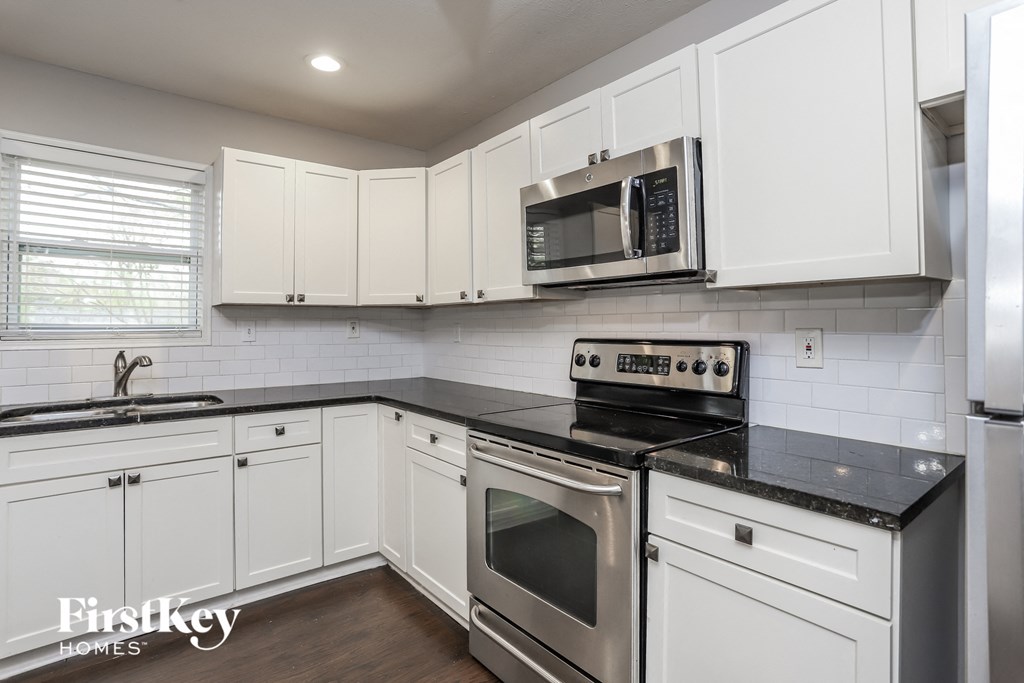 A kitchen with white cabinets and black countertops.
