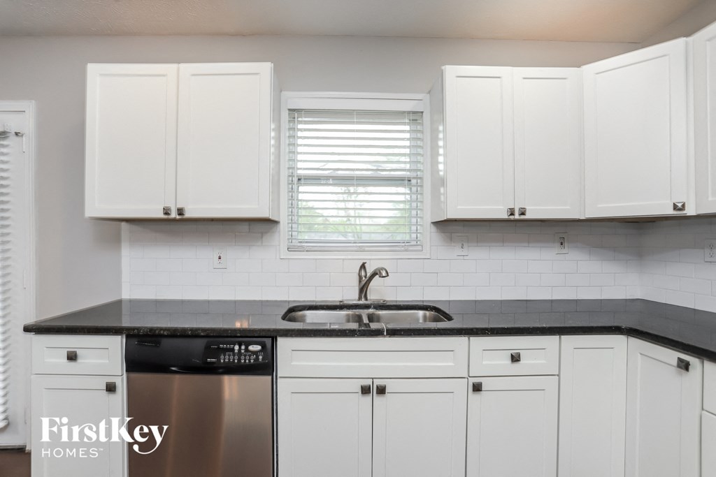 A kitchen with white cabinets and a black countertop.