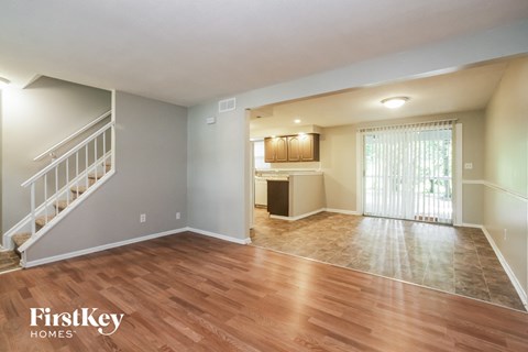 an empty living room with a staircase and a kitchen
