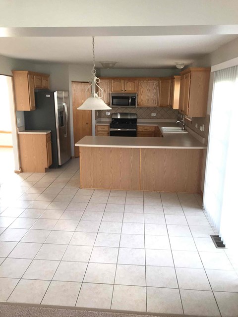 an empty kitchen with wooden cabinets and a white tiled floor