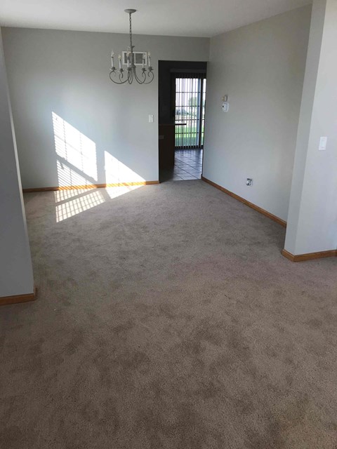 an empty living room with carpet and a chandelier
