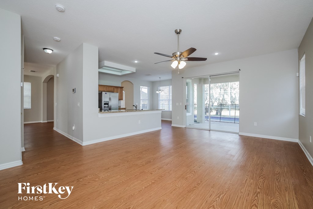 an empty living room and kitchen with wood flooring and a ceiling fan