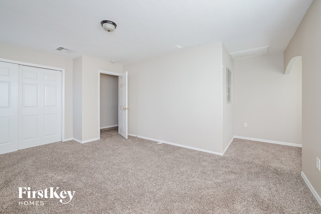 a bedroom with white walls and carpet and a door to a closet