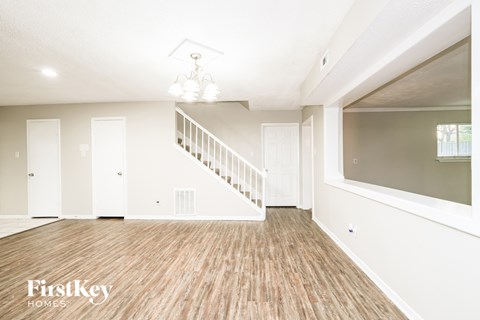 A spacious room with wooden flooring and a staircase.