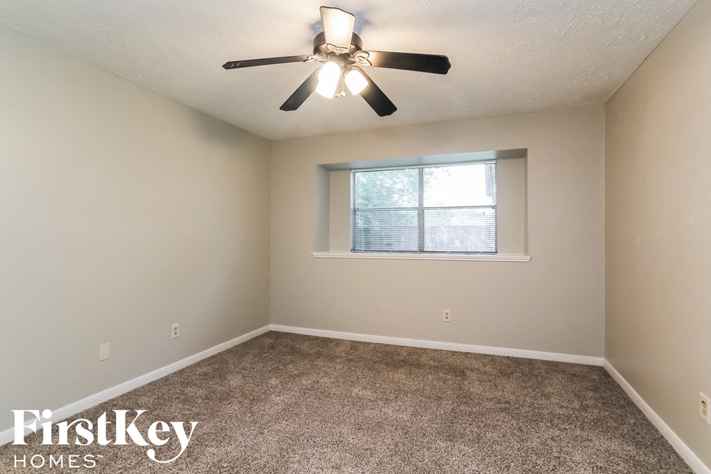 the spacious bedroom with carpeted flooring and a ceiling fan