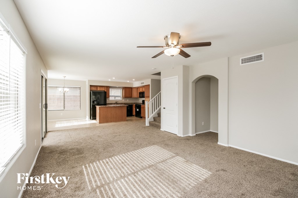 an empty living room with a ceiling fan and a kitchen