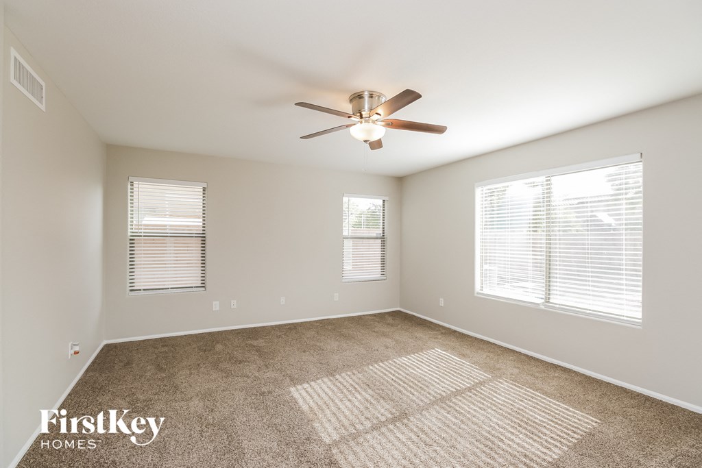 an empty living room with a ceiling fan and two windows