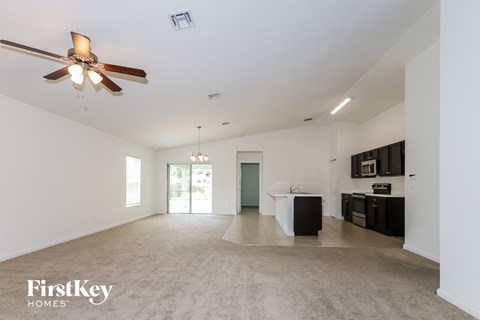 A spacious living room with a ceiling fan and a kitchen area in the background.