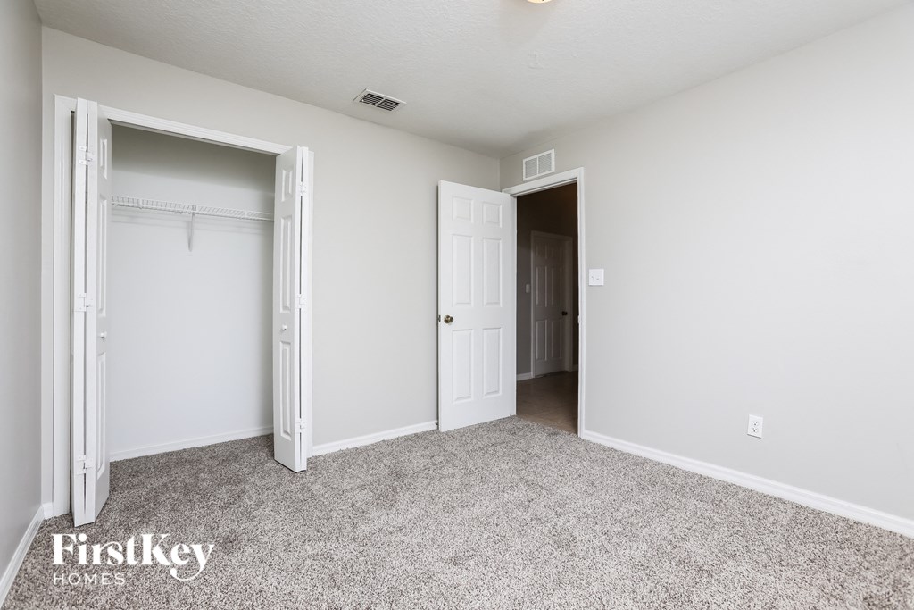 a bedroom with white walls and carpet and a door to a closet