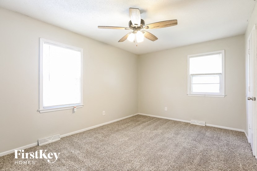 an empty room with a ceiling fan and two windows