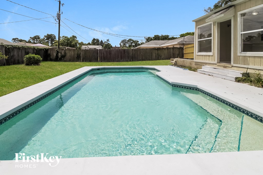 A swimming pool in a backyard with a house and fence in the background.