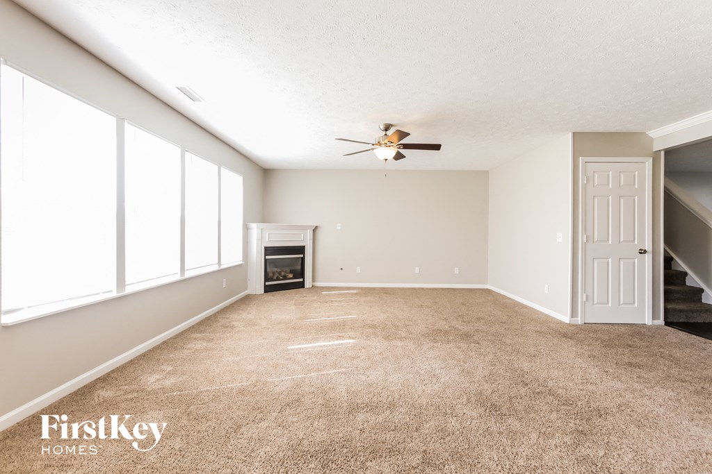 a carpeted living room with a ceiling fan and a fireplace