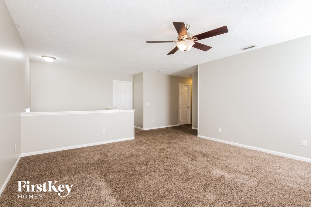 a spacious living room with carpet and a ceiling fan