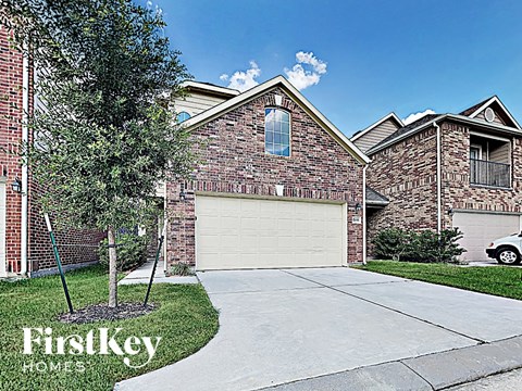 A brick house with a garage door and a tree in front.