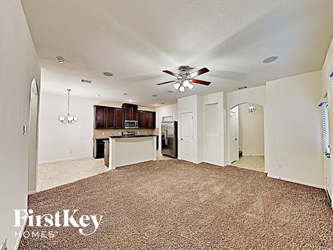 A carpeted room with a ceiling fan and a kitchen area in the background.