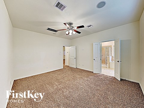 A carpeted room with a ceiling fan and a doorway leading to another room.