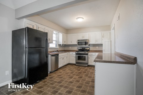 A kitchen with a black fridge and brown tiled floor.