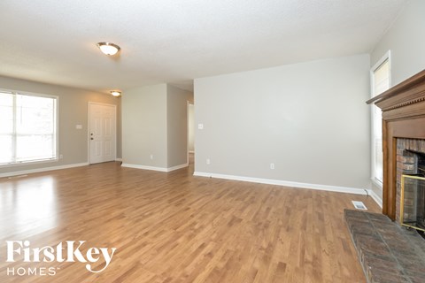 A spacious room with wooden flooring and a fireplace on the right side.