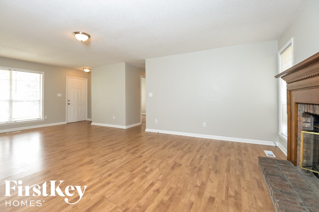 A spacious room with wooden flooring and a fireplace on the right side.