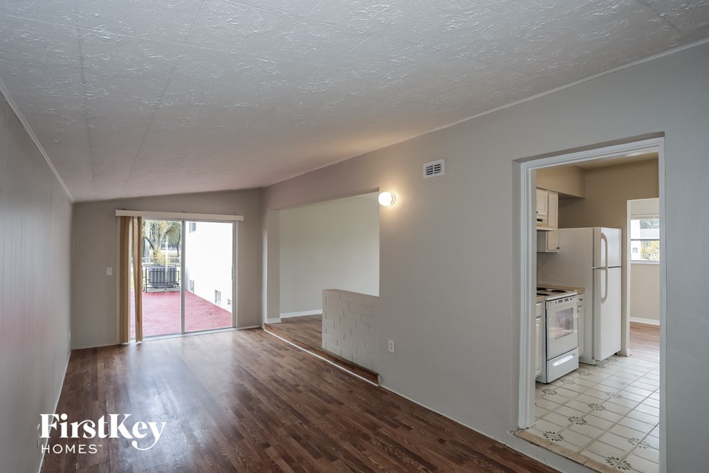 an empty living room and kitchen with wood flooring and a door to a patio