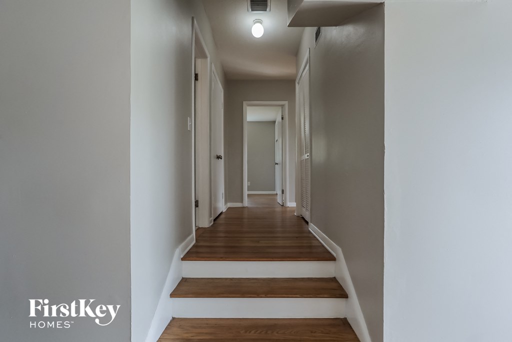 a long hallway with stairs and wood flooring and white walls