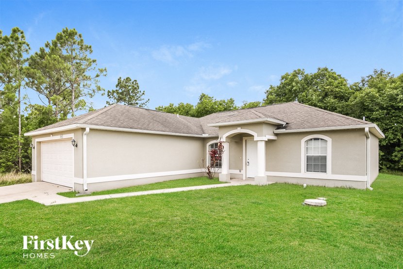 a beige house with a green lawn and trees
